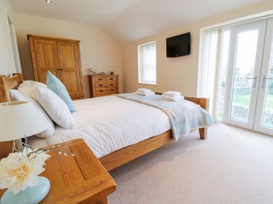 A bedroom with a wooden bed and furniture and a television mounted on the wall at Tyn Y Buarth in Dyffryn Ardudwy