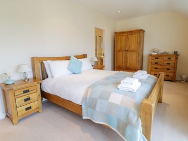 A bedroom with a wooden bed with white bedding and blue checkered blanket two wooden bedside tables lamp and flowers wooden wardrobe and chest of drawers at Tyn Y Buarth in Dyffryn Ardudwy
