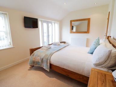 A bedroom with a wooden bed a mounted TV and a large mirror at Tyn Y Buarth in Dyffryn Ardudwy