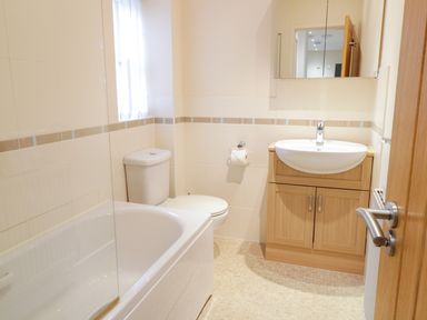 A bathroom with a bathtub a toilet a sink with wooden cabinet and a mirror at Tyn Y Buarth in Dyffryn Ardudwy