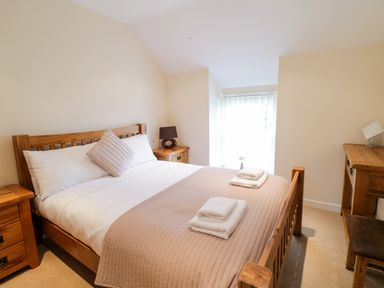 A bedroom with a wooden bed with white and beige bedding a wooden nightstand a lamp a wooden desk and a chair at Tyn Y Buarth in Dyffryn Ardudwy