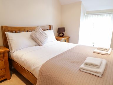 A bedroom with a wooden bed and side tables with a lamp and folded towels on the bed at Tyn Y Buarth in Dyffryn Ardudwy