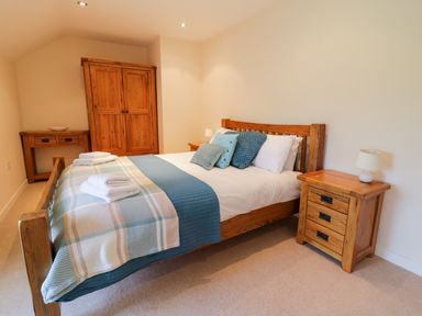 A bedroom with a wooden bed with pillows and folded towels a wooden wardrobe a wooden bedside table with a lamp and a wooden desk at Tyn Y Buarth in Dyffryn Ardudwy