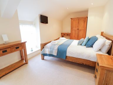 A bedroom with a wooden bed with blue bedding wooden desk and wardrobe and a wall-mounted television at Tyn Y Buarth in Dyffryn Ardudwy