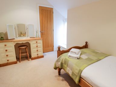 A bedroom with a single wooden bed with folded towels and a green checkered blanket a dressing table with mirrors and a stool at Tyn Y Buarth in Dyffryn Ardudwy