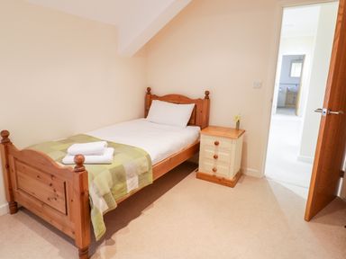 A bedroom with a single wooden bed with white bedding and a green checkered blanket and a bedside table with a small vase at Tyn Y Buarth in Dyffryn Ardudwy
