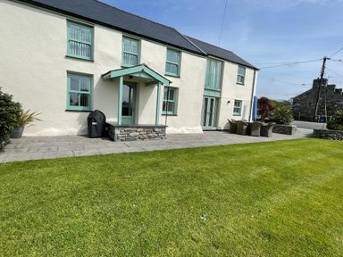 The exterior of a two story house with green framed windows a door and patio furniture on the side at Tyn Y Buarth in Dyffryn Ardudwy