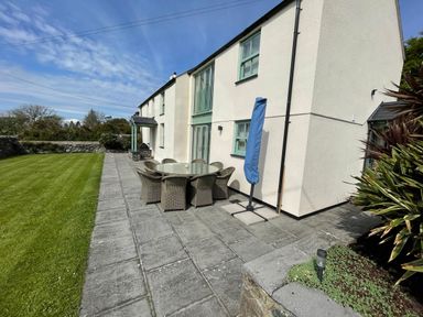 An outdoor patio with a glass table and wicker chairs beside a white house with green window frames at Tyn Y Buarth in Dyffryn Ardudwy