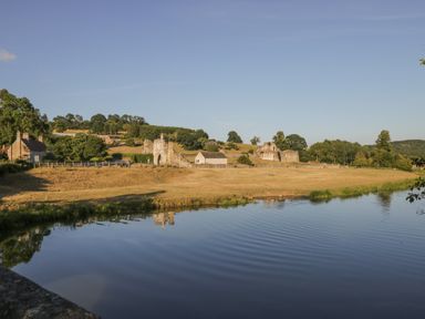 A river with ripples in front of grassy land with historic stone structures and trees at Sykes Lodge in Malton