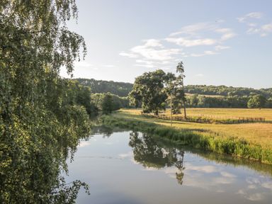 A river with trees and fields under a partly cloudy sky at Sykes Lodge in Malton