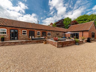 A courtyard with gravel ground surrounded by brick buildings with tiled roofs and garden furniture at Sykes Lodge in Malton