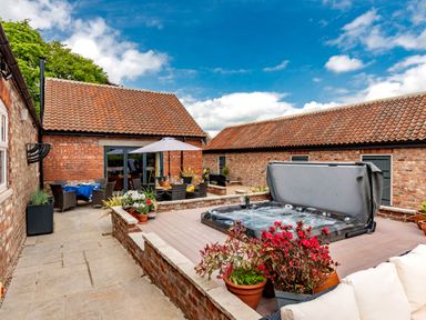 An outdoor patio area with a hot tub dining tables and potted plants at Sykes Lodge in Malton