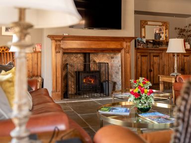A living room with a wood-burning stove inside a wooden fireplace and glass tables with flowers at Sykes Lodge in Malton