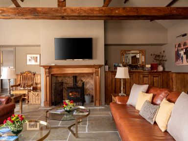 A living room with a leather sofa pillows glass coffee tables a fireplace a tv and wooden beams at Sykes Lodge in Malton