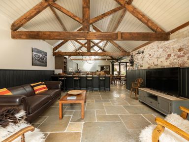 A living room with a leather sofa wooden coffee table large television and exposed wooden beams at Sykes Lodge in Malton