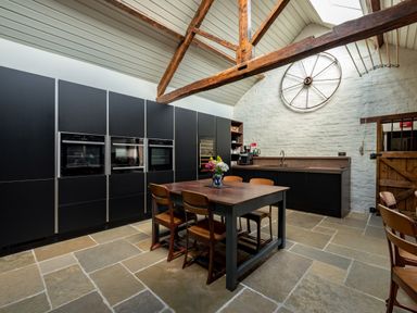 A kitchen with black cabinets wooden table and chairs stone floor and vintage wheel on white brick wall at Sykes Lodge in Malton