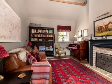 A sitting room with a leather couch, bookshelf, red patterned rug, wooden desk, armchair, and a fireplace at Sykes Lodge in Malton