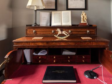 A wooden desk with open compartments holding papers and drawers with a lamp book and decorative items on top at Sykes Lodge in Malton