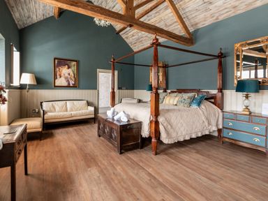 A bedroom with a four-poster bed sofa wooden chest dresser with lamps and a portrait on the wall at Sykes Lodge in Malton