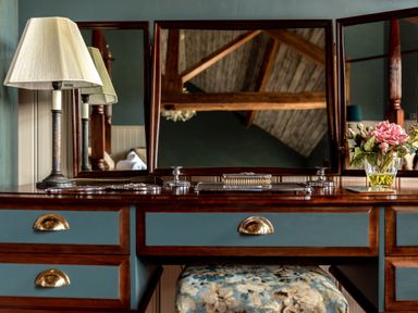 A wooden dressing table with mirrored panels a lamp and flowers at Sykes Lodge in Malton
