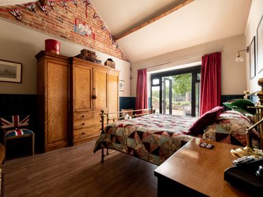 A bedroom with a brass bed a wooden wardrobe red curtains and a chair with a union jack cushion at Sykes Lodge Malton