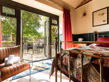 A bedroom with a brass bed and patchwork quilt next to an open glass door leading to an outdoor seating area at Sykes Lodge in Malton