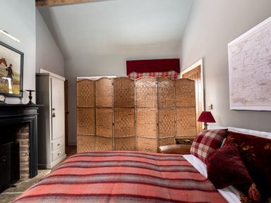 A bedroom with a bed covered by a striped blanket and pillows a wooden room divider a fireplace and framed pictures at Sykes Lodge in Malton