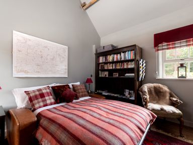 A bedroom with a bed covered in a striped blanket and pillows a bookshelf an armchair with a fur throw and a window at Sykes Lodge in Malton