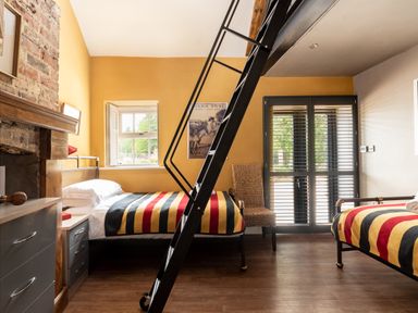 A bedroom with two single beds with striped blankets a chair a window and a metal ladder at Sykes Lodge in Malton