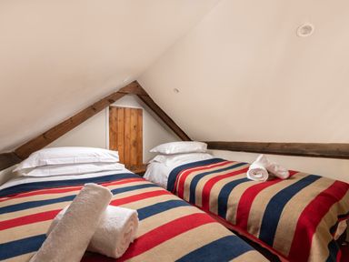 A small attic bedroom with two single beds with striped blankets and white towels at Sykes Lodge in Malton
