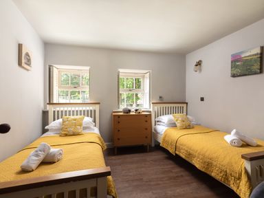 A bedroom with two single beds with yellow bedspreads and pillows a wooden chest of drawers between the beds and two windows behind the beds at Sykes Lodge in Malton