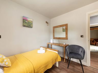 A bedroom with a single bed with yellow bedding a wooden table with a mirror above and a gray chair at Sykes Lodge Malton