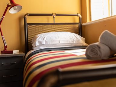 A single bed with striped bedding and white pillows next to a nightstand with a red lamp and a book at Sykes Lodge in Malton