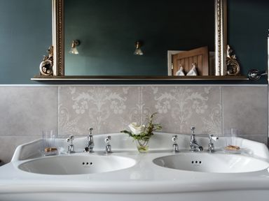 A bathroom double sink with chrome faucets a flower arrangement on the counter and a large framed mirror on the wall at Sykes Lodge in Malton