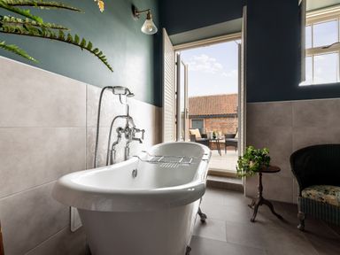 A bathroom with a freestanding bathtub near open doors leading to an outdoor patio with chairs and a table at Sykes Lodge Malton