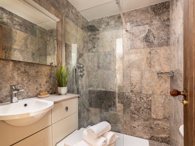 A bathroom with a sink cabinet, mirror, shower area, and rolled towels at Sykes Lodge in Malton