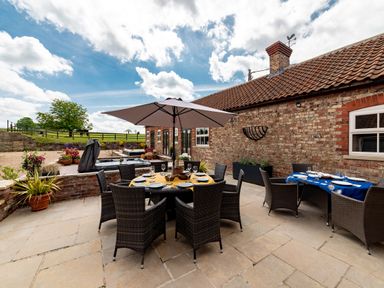 An outdoor patio with two dining tables and chairs a large umbrella and potted plants at Sykes Lodge in Malton