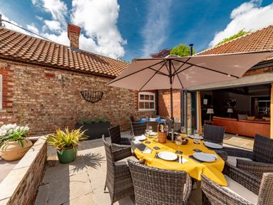 An outdoor patio with a round table set for dining under a large umbrella at Sykes Lodge in Malton