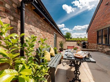 An outdoor patio area with a bench and table set with breakfast items between brick buildings at Sykes Lodge Malton