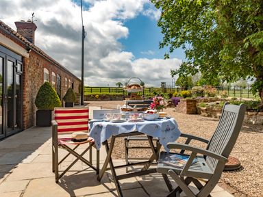 An outdoor patio with a table set for tea with chairs beside a brick building and garden at Sykes Lodge in Malton