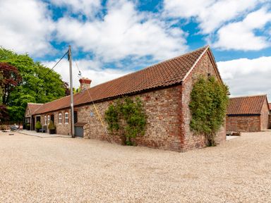 An exterior view of a brick building with a tiled roof and gravel ground at Sykes Lodge in Malton