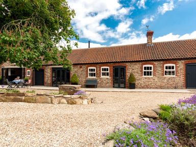 A brick house with tiled roof gravel yard purple flowers and outdoor seating at Sykes Lodge in Malton