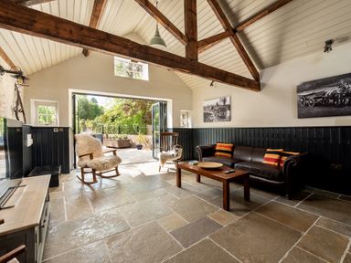 A living room with wooden beams a leather sofa rocking chairs and an open door to a garden at Sykes Lodge in Malton