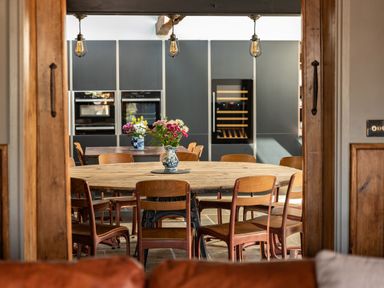 A kitchen with a round wooden table and wooden chairs with flowers in a vase on the table at Sykes Lodge in Malton