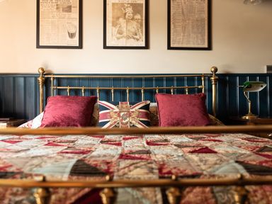 A bedroom with a brass bed frame red pillows a Union Jack cushion and framed newspaper clippings on the wall at Sykes Lodge in Malton