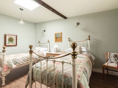 A bedroom with two single beds with patterned quilts a wooden nightstand and a chair with cushions at Sykes Lodge in Malton