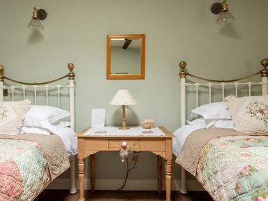 A bedroom with two single beds separated by a wooden bedside table with a lamp and small decor items at Sykes Lodge in Malton