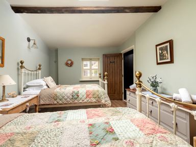 A bedroom with two metal beds with patchwork quilts a wooden dresser with flowers and rolled towels and a wooden door at Sykes Lodge in Malton
