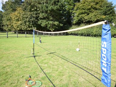 A badminton net set up on grass with two rackets and a croquet set in the background at Sykes Lodge in Malton