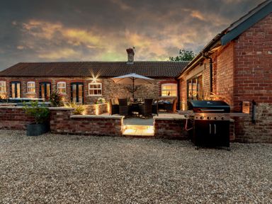 An outdoor patio with a dining table under an umbrella a grill and brick walls at Sykes Lodge in Malton